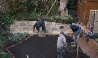 Un aperçu de la transformation d'un petit jardin londonien en cours, y compris un ouvrier posant des dalles York Stone pour une terrasse à l'arrière du jardin.