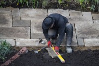 Un ouvrier préparant une dalle de York Stone à utiliser sur une terrasse lors de la rénovation d'un petit jardin londonien.