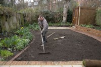 Un ouvrier ratissant le sol en vue de la pose d'un nouveau gazon lors de la rénovation d'un jardin londonien.