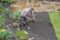 Un travailleur de jardin ratissant le sol en vue de la pose de gazon lors d'une rénovation de jardin.