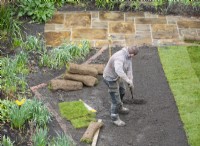 Un travailleur de jardin ratissant le sol en vue de la pose de gazon lors d'un relooking de garen.