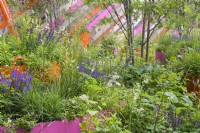 Grande jardinière orange remplie d'eau et de plantes aquatiques et entourée de vivaces - The St Mungo's Putting Down Roots Garden