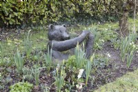 Une sculpture d'ours en résine de bronze se trouve dans un parterre de fleurs d'hiver. Sculpture réalisée par Suzi Marsh. Février.