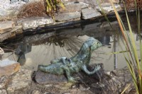 Céramique, lézard vert, fabriqué par Evelyn Perkins, à côté d'un étang. Février.