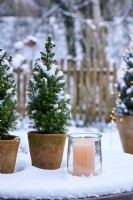 Arrangement de table de Picea glauca 'Conica' dans un pot en céramique entouré de neige et d'une bougie avec vue sur le jardin enneigé
