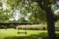 Balançoire suspendue à un arbre mature dans la section pelouse du jardin. Parterres informels en arrière-plan. Été.
