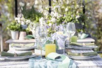 Table dressée dans une serre avec assiettes, couverts, verres, bougies et un présentoir de fleurs au milieu