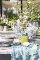 Table dressée dans une serre avec assiettes, couverts, verres, bougies et un présentoir de fleurs au milieu