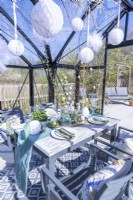 Table dressée dans une serre avec assiettes, couverts, verres, bougies et un présentoir de fleurs au milieu avec des décorations de Pâques