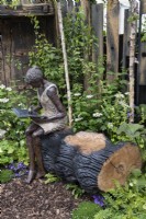 Sculpture en bronze d'une femme intitulée 'Belle' assise sur un rondin de chêne noirci.Dawn Conn Sculpture stand au RHS Chelsea Flower Show 2023