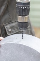 Femme forant des trous de drainage dans le fond du pot en métal
