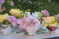 Roses roses et jaunes affichées dans des tasses à thé en porcelaine vintage sur un plateau peint