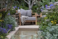 Une chaise surplombe un ruisseau bordé d'armoises à feuilles grises, d'iris, d'ombellifères et d'herbes.