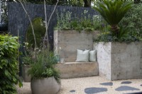 Un jardin de patio urbain avec des sièges et des pots créés à partir d'hypertufa léger et planté de plantes résistantes à la sécheresse. Un miroir reflète la plantation, donnant une illusion d'espace supplémentaire.