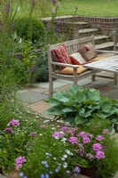 Patio en contrebas avec table, siège et coussins et plates-bandes surélevées de plantes vivaces. Étapes menant à la pelouse à un niveau supérieur - Open Gardens Day, Tuddenham, Suffolk