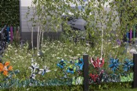 Une façon ludique de recycler les déchets de sacs en plastique en les tissant dans la clôture en grillage. Derrière, un bosquet de bouleaux et une prairie de fleurs sauvages et d'herbes.