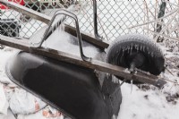 Brouette en métal noir stockée recouverte de glace dans l'arrière-cour après une tempête de pluie verglaçante au début du printemps.