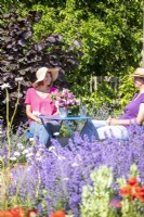 Les femmes discutant assis à table dans le jardin au-delà des fleurs