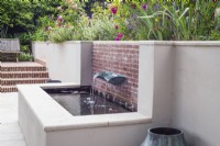 Enduit blanc et piscine surélevée en briques avec fontaine bassin vert-de-gris avec parterres de fleurs au-dessus