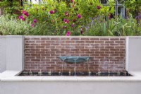 Fontaine bassin vert-de-gris sur mur de briques d'eau en rendu surélevé avec terrasse fleurie avec roses au-dessus.