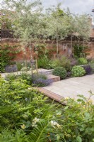 Jardin clos de murs avec dallage en grès, petit bassin bordé de briques, moustiquaire Pyrus salicifolia 'Pendula' et petits parterres secs