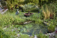 Bassin de jardin surplombé par un héron décoratif en métal en juillet