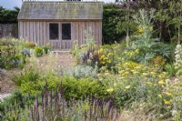 Cabanon en bois dans jardin de gravier avec plantation mixte comprenant : Lonicera nitida 'Maigrum'; Cardon; Artemisia 'Powis Castle'; Achillée 'Moonshine