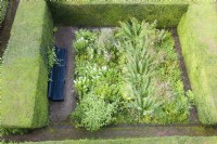 Vue sur jardin clos de haies d'ifs taillés, planté de plantes vivaces à floraison tardive avec long banc peint en noir. Septembre. Image prise avec un drone.