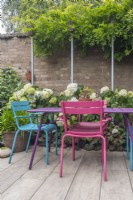 Table et chaises colorées sur un petit jardin urbain clos et pavé avec supports de poteaux d'échafaudage avec glycine et hortensia 'Annabelle'