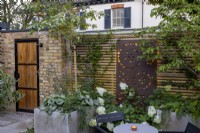 Jardin de cour au crépuscule avec parterres de fleurs surélevés et clôture en bois contemporaine avec écran métallique décoratif rétro-éclairé près du coin salon