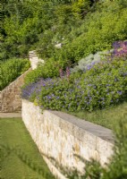Mur de soutènement en pierre avec un parterre de plantes vivaces à fleurs, été août