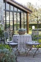 Salon de jardin en métal blanc décoré d'une nappe et d'un panier en métal planté d'Altos.