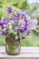 Bouquet de fleurs contenant Gypsophila elegans 'Covent Garden', Salvia viridis 'Blue Monday', Briza maxima, Lathyrus 'Matucana' et 'Midnight Blues' Sweet Peas dans un vase en verre enveloppé de corde