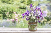 Bouquet de fleurs contenant Gypsophila elegans 'Covent Garden', Salvia viridis 'Blue Monday', Briza maxima, Lathyrus 'Matucana' et 'Midnight Blues' Sweet Peas dans un vase en verre enveloppé de corde
