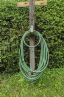 Tuyau d'arrosage de jardin vert enroulé sur un support métallique fixé à un poteau en bois dans la cour en été.
