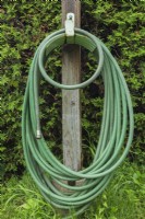 Tuyau d'arrosage de jardin vert enroulé sur un support métallique fixé à un poteau en bois dans la cour en été.