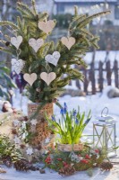Arrangement hivernal extérieur avec couronne, muscari en pot et branches d'épinette décorées de coeurs en bois.