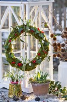 Arrangement hivernal avec perce-neige en pot et bouquet de perce-neige dans un vase et une couronne composée de mousse, perce-neige, rose de Gueldre et gui.