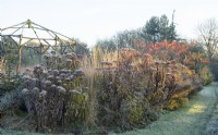 Gazebo rustique en bois givré entouré de plantes vivaces en décomposition et de graminées ornementales en hiver