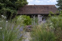 Petit jardin intérieur rempli de plantations de fin d'été, avec un bâtiment à charpente en chêne derrière.