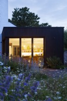 Vue sur les parterres de fleurs et la pelouse de la maison et l'extension de la cuisine moderne au crépuscule.
