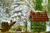 Parus major - Mésange charbonnière sur une souche d'arbre mangeant des graines de tournesol et une mangeoire à oiseaux en bois colorée sur le balcon en hiver. vue du balcon sur le jardin.