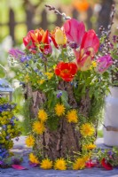 Bouquet de fleurs printanières comprenant des fleurs sauvages et des tulipes dans un vase recouvert d'écorce. Couronne composée de fleurs de pissenlit.