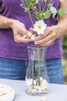 Femme plaçant des pierres dans un vase avec des anémones blanches pour les maintenir en place