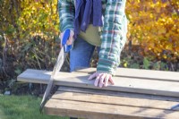 Femme sciant les extrémités des planches de bois pour qu'elles mesurent un mètre de long