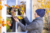 Femme plaçant une couronne faite de lierre, de brins de hêtre et d'aubépine sur une porte