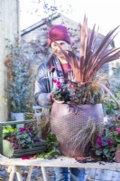 Femme plantant du Cyclamen en pot avec Cordyline 'Red Star', Carex 'Bronco' et Leucothoe 'Zeblid'