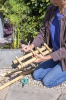 Femme attachant des morceaux de bambou plus courts entre deux morceaux plus longs pour créer une petite échelle