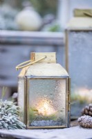 Petites lanternes avec de l'eau sur verre provenant du gel fondu avec des brins de pin et des pommes de pin sur des caisses en bois - couvertes de givre