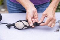 Femme attachant tous les morceaux de ficelle en un seul nœud au-dessus du galet pour le maintenir en place